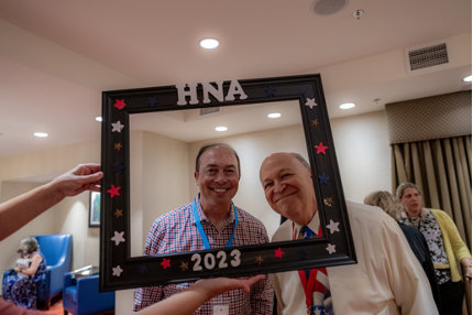 Two men pose with the frame that someone else is holding